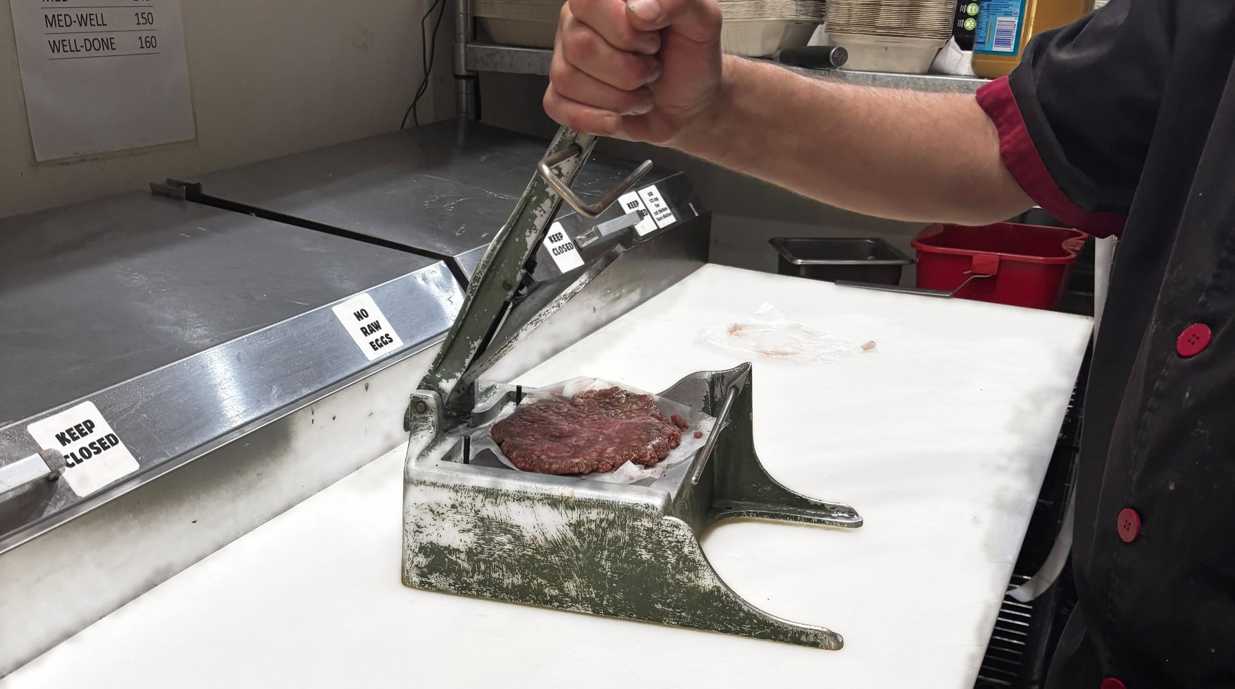 A beef patty being pressed by hand in the Broken Barrel kitchen